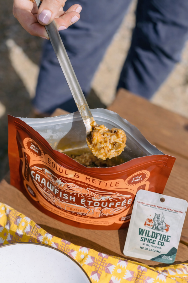 Person using a spoon to serve crawfish étouffée from a Bowl & Kettle package with a Wildfire Spice Co. tag.